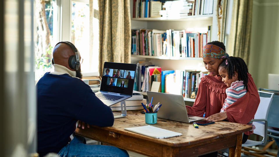 A man working from home while his wife and daughter work on a computer opposite