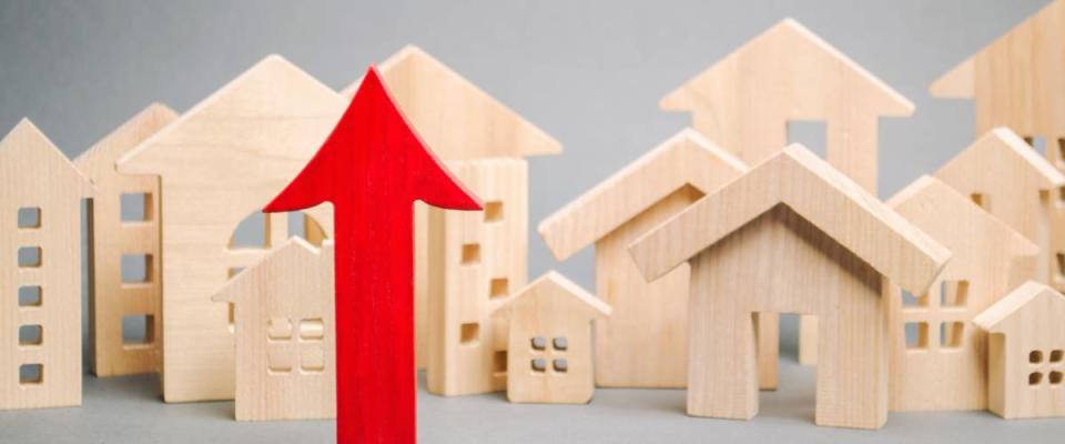 Red arrow up and miniature wooden houses. The concept of rising property prices.