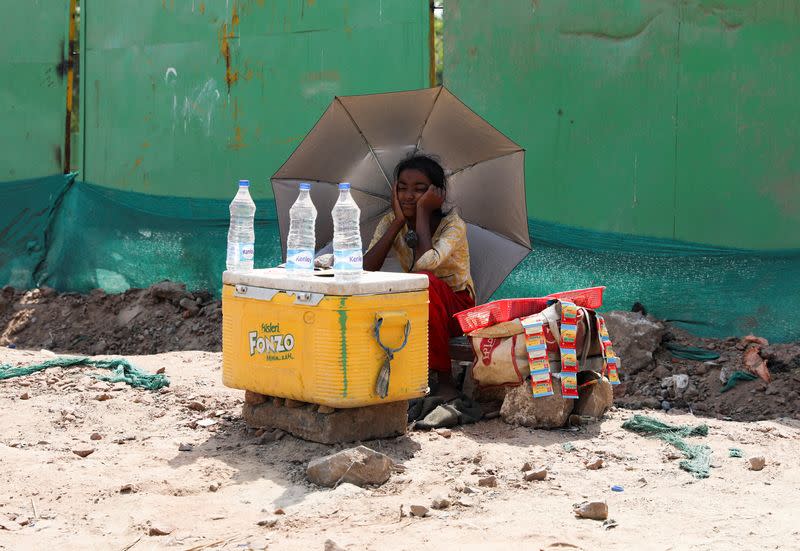 A girl selling water uses an umbrella to protect herself from the sun as she waits for customers on a hot summer day, in New Delhi