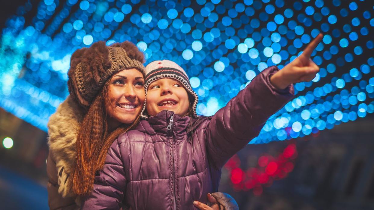 cheerful young woman and her daughter are having fun in the city street at christmas time