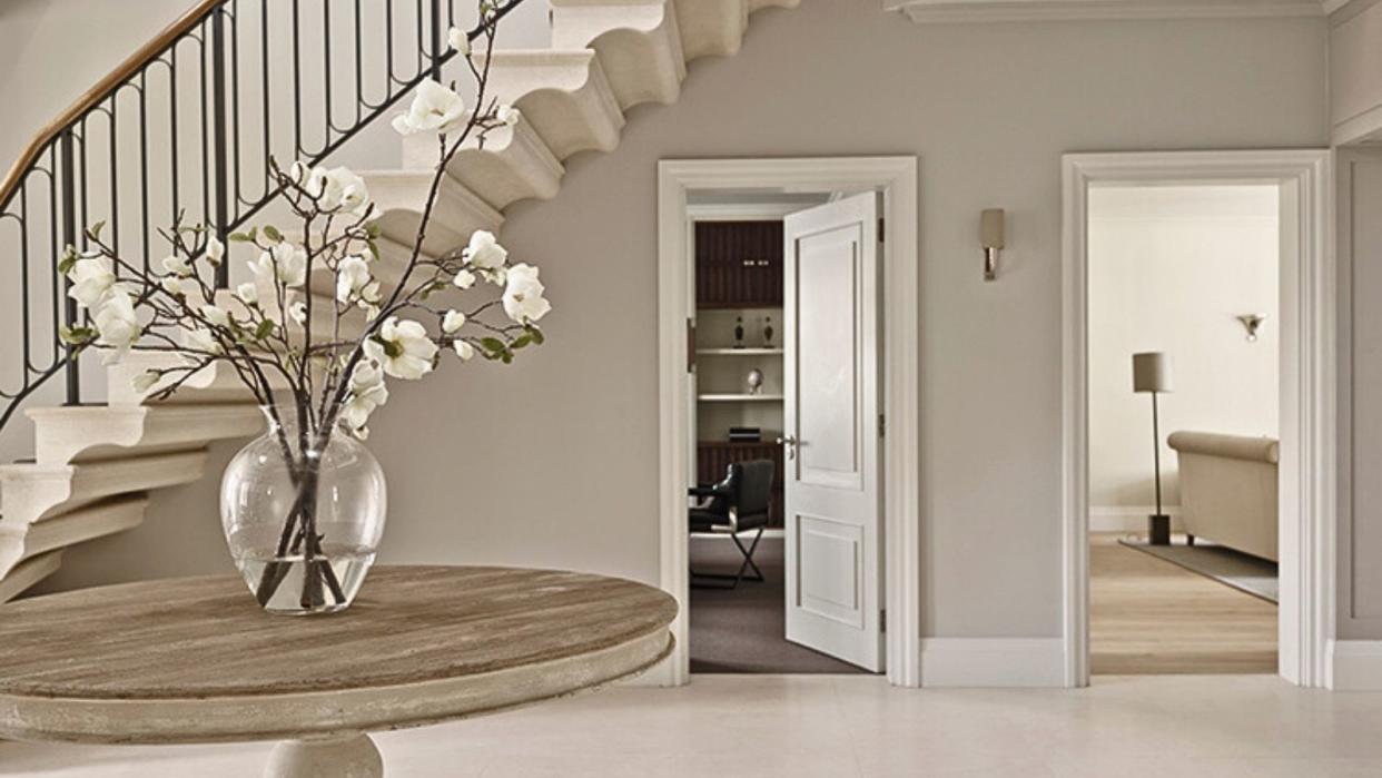  A large neutral colored entryway with a large center table with a vase of orchids, and an open door under the stairs leading to a home office 