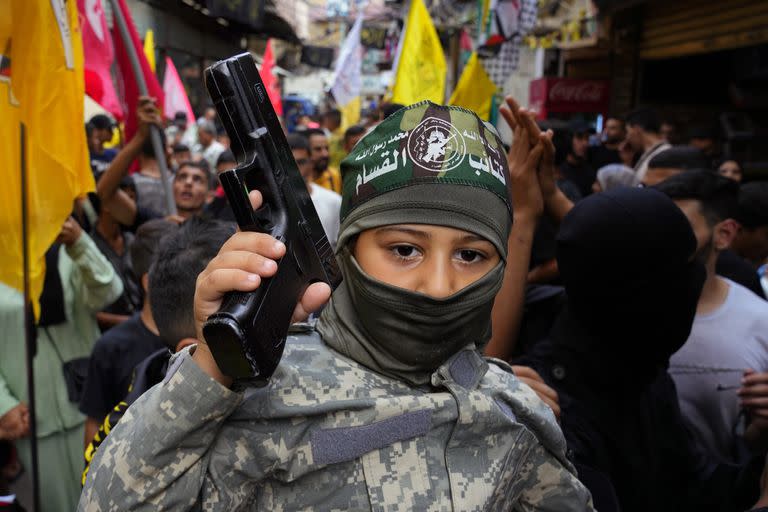Un niño palestino vestido con uniforme militar sostiene un arma mientras otros bailan para celebrar los ataques que el grupo militante Hamas llevó a cabo contra Israel, en el campo de refugiados palestinos de Bourj al-Barajneh, en Beirut, Líbano, el sábado 7 de octubre de 2023