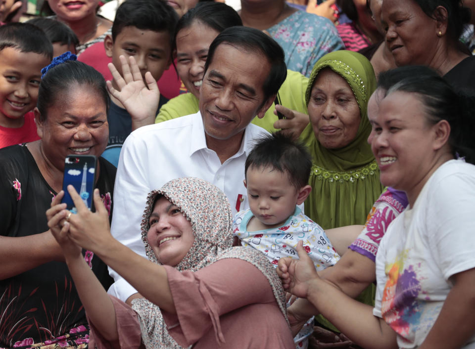 Residents take a selfie with incumbent Indonesian President Joko Widodo, center, prior to a speech declaring his victory in the country's presidential election, at a slum in Jakarta, Indonesia, Monday, Tuesday, May 21, 2019. Indonesian President Joko Widodo has been elected for a second term, official results showed, in a victory over a would-be strongman who aligned himself with Islamic hard-liners and vowed Tuesday to challenge the result in the country's highest court. (AP Photo/Dita Alangkara)