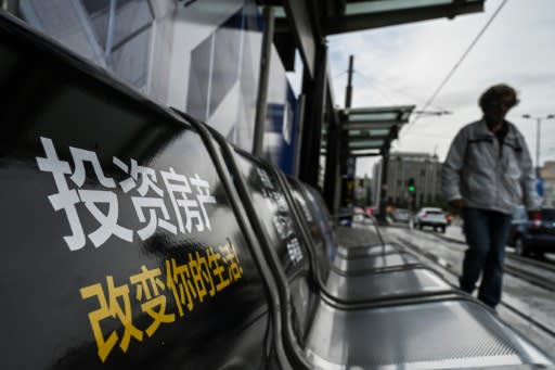 A man walks past seats at a tram station decorated with Golden visa advertisements aiming Chinese clientele