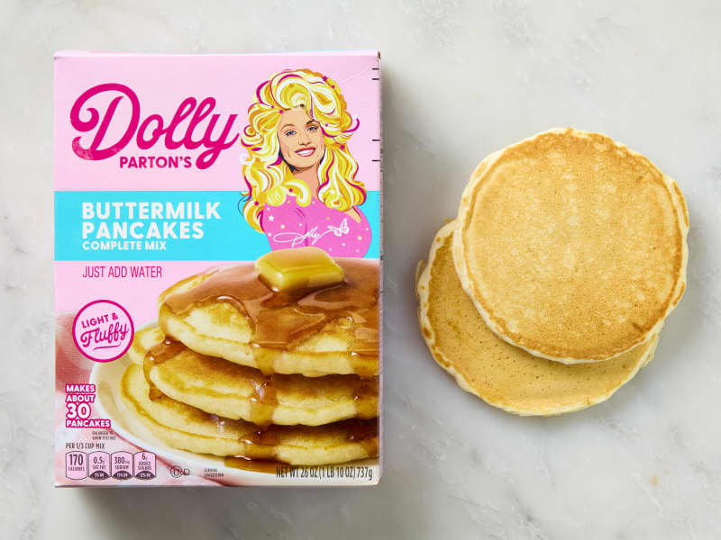 overhead shot of a box of dolly parton pancake mix, with two pancakes to the right of it.
