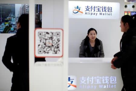 A sales assistant sits behind and under Alipay logos at a train station in Shanghai, February 9, 2015. REUTERS/Aly Song/File Photo