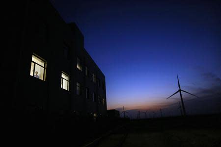 A man stands at the window of a building near a wind turbine used to generate electricity, at a wind farm in Guazhou, 950km (590 miles) northwest of Lanzhou, Gansu Province September 15, 2013. REUTERS/Carlos Barria