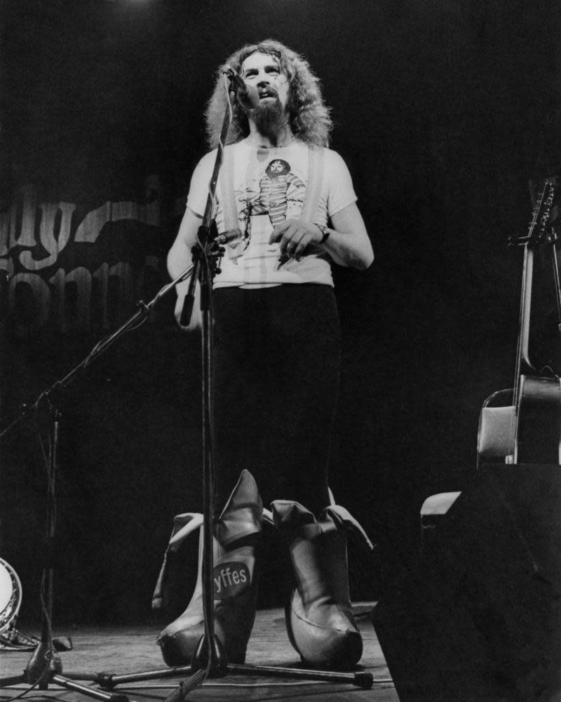 Scottish comedian Billy Connolly performing on stage in a pair of outsize, banana-shaped boots, 1977.  