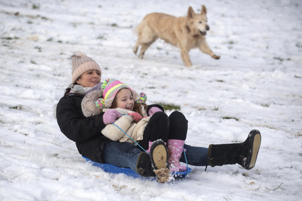 Lizzy and daughter Connie, 6, are chased down a snow covered hill by their golden retriever Pippa in a park in Newcastle-under-Lyme, England, Monday, Dec. 28, 2020. In the aftermath of Storm Bella swathes of the UK are braced for a cold snap, with snow and ice warnings in force across the country. (Joe Giddens/PA via AP)