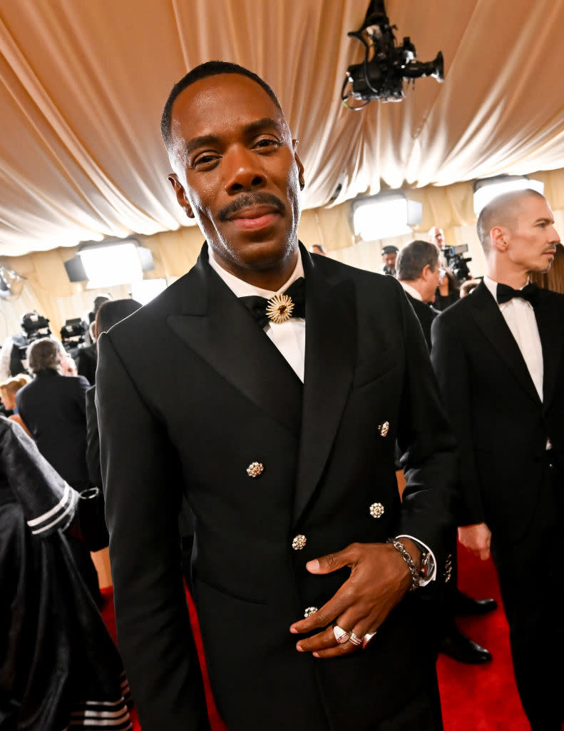 Man in a double-breasted suit with a unique flower brooch, posing at an event