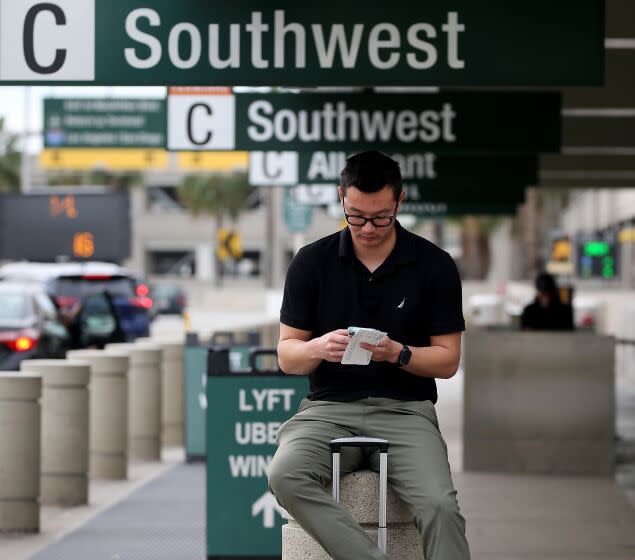 SANTA ANA, CALIF. - DEC. 27, 2022. Kenneth Zhou waits for a ride at John Wayne Airport on Tuesday, Dec. 27, 2022, after a three-day journey from Phoenix because of delays, layovers and cancelations by Southwest Airlines. The budget carrier has canceled thousands of flights over the Christmas holidays . (Luis Sinco / Los Angeles Times)
