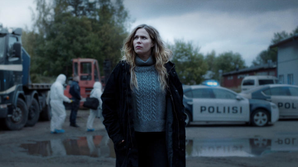 closeup of a woman standing in front of a crime scene, looking away