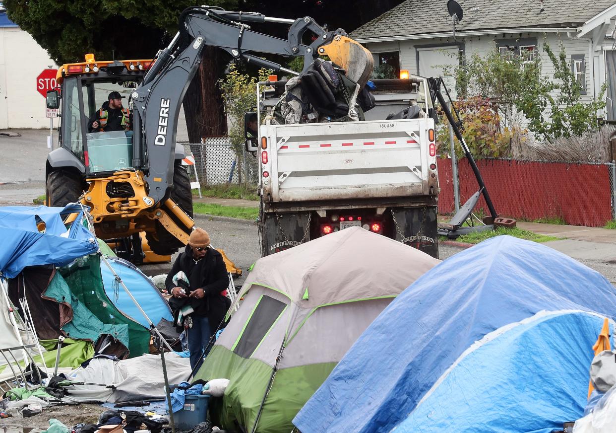 A person rummages through an encampment tent as a Bremerton City backhoe scoops up items left behind and puts them into a dump truck on MLK Way in Bremerton on Saturday.