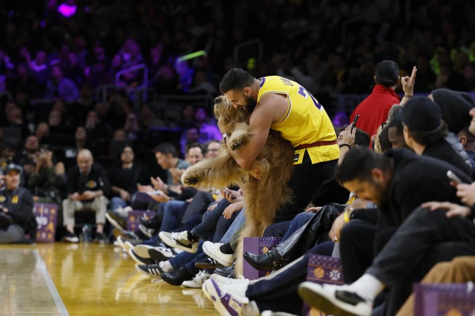 Cliff Brush Jr. hugs Brodie the Goldendoodle as they sit courtside at the Lakers-Knicks game.