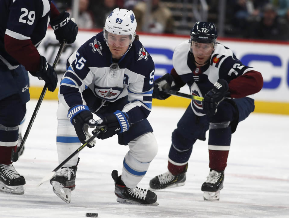 Winnipeg Jets center Mark Scheifele, front, reaches out to control the puck as Colorado Avalanche right wing Joonas Donskoi defends during the second period of an NHL hockey game Tuesday, Dec. 31, 2019, in Denver. (AP Photo/David Zalubowski)