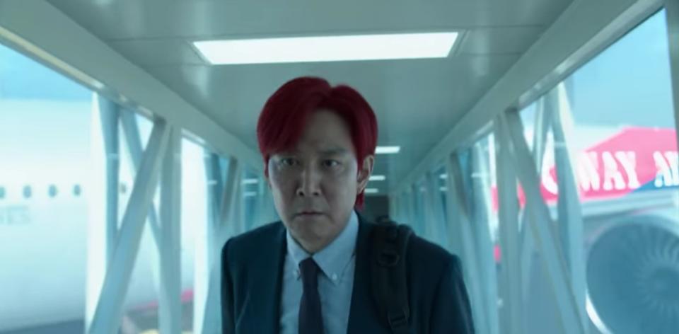 A red-haired Gi-hun looks determined while walking up a tunnel away from an airplane