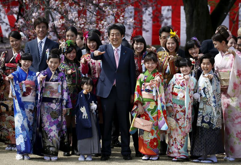 FILE PHOTO: Japan's PM Abe poses with child actors, members of Japanese idol group Momoiro Clover Z and other show-business celebrities at a cherry blossom viewing party at Shinjuku Gyoen park in Tokyo