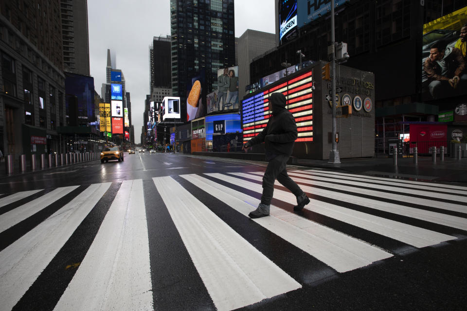 A man crosses the street in a nearly empty Times Square, which is usually very crowded on a weekday morning, Monday, March 23, 2020 in New York. Gov. Andrew Cuomo has ordered most New Yorkers to stay home from work to slow the coronavirus pandemic. (AP Photo/Mark Lennihan)