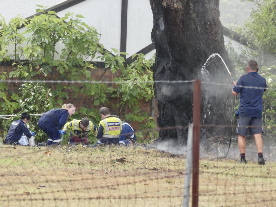 The woman and a tree was struck by lightning before another strike on Sydney's Northern Beaches 10 minutes later. Pictured are medical staff at the scene and a man with a hose putting the fire out at a tree.