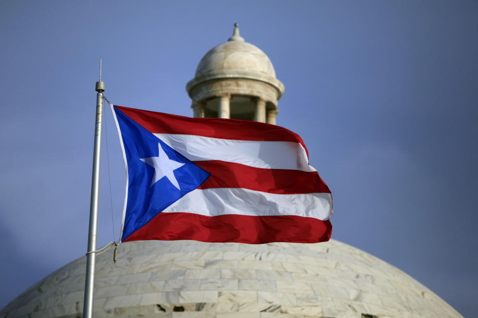 FILE - In this July 29, 2015 file photo, the Puerto Rican flag flies in front of Puerto Rico's Capitol as in San Juan, Puerto Rico. A federal control board that oversees Puerto Rico’s finances approved on Wednesday, July 1, 2020, a new budget that largely suspends austerity measures and government cuts for one year as the U.S. territory struggles to recover from hurricanes, earthquakes and the pandemic. (AP Photo/Ricardo Arduengo, File)