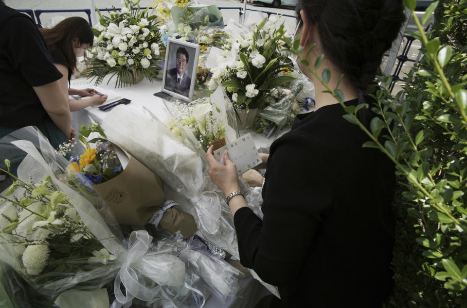 A staffer, right, moves bouquets of flowers to make room as a woman writes her name and a message after laying a bouquet of flowers at a designated stand set up for former Japanese Prime Minister Shinzo Abe at the Liberal Democratic Party's headquarters in Tokyo on Monday, July 11, 2022. Abe was assassinated Friday while campaigning in Nara, western Japan. (AP Photo/Hiro Komae)