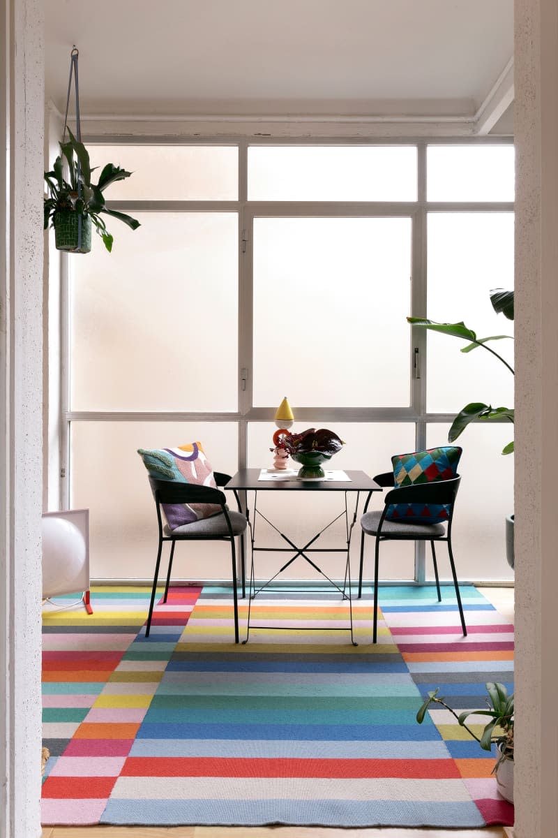 Cafe table and chairs in room with frosted windows and rainbow striped rug.