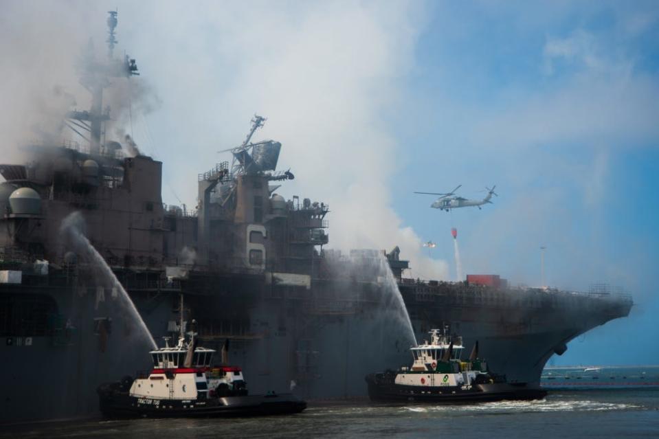 An MH-60S Seahawk helicopter from the “Merlins” of Helicopter Sea Combat Squadron (HSC) 3, provides aerial firefighting support alongside Sailors and civilian fire crews on the ground to fight the fire aboard amphibious assault ship USS Bonhomme Richard (LHD 6)