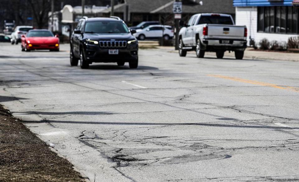 Vehicles travel near rough road along Washington Street, Tuesday, April 12, 2022, in Manitowoc, Wis. There are plans to rebuild the well-traveled road.