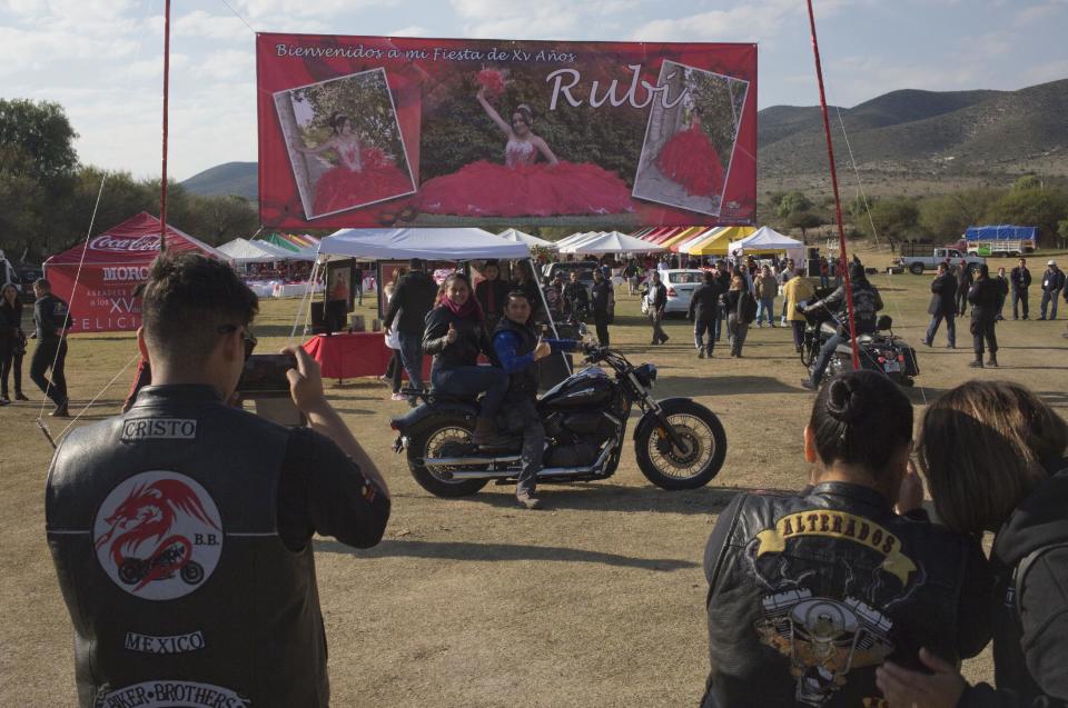 A couple, who traveled from Mexico City with a group of bikers, pose for a photo backdropped by a banner welcoming visitors to Rubi Ibarra's down-home 15th birthday party in the village of La Joya, San Luis Potosi State, Mexico, Monday, Dec. 26, 2016. Millions of people responded to the invitation for Rubi's Dec. 26th coming of age party in rural northern Mexico, after her parent's video asking "everybody" to attend went viral. (AP Photo/Enric Marti)