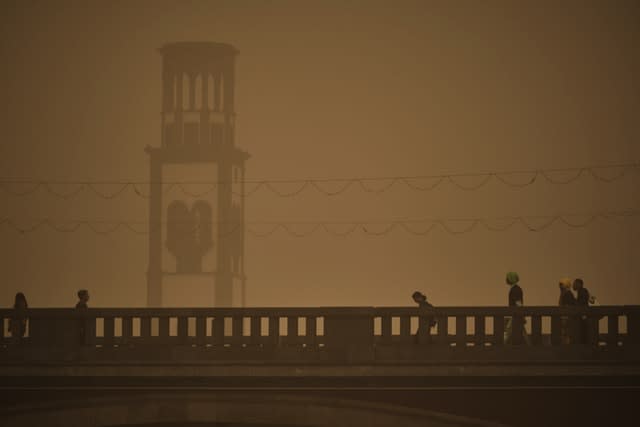 People walk across a bridge in a cloud of red dust