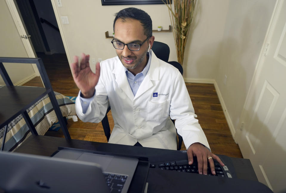 Medical director of Doctor on Demand Dr. Vibin Roy waves good-bye to a patient at the conclusion of an online primary care visit conducted from his home, Friday, April 23, 2021, in Keller, Texas. Some U.S. employers and insurers want you to make telemedicine your first choice for most doctor visits. Retail giant Amazon and several insurers have started or expanded virtual-first care plans to get people thinking telemedicine routinely, even for annual checkups. (AP Photo/LM Otero)