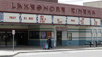 A woman wearing a mask walks with her groceries past a closed Lakeshore Cinema theatre, Wednesday, May 6, 2020, in Euclid, Ohio. With the economy paralyzed by business closures, the unemployment rate likely jumped to at least 16% — from just 4.4% in March — and employers cut a stunning 21 million or more jobs just in April, economists have forecast. (AP Photo/Tony Dejak)