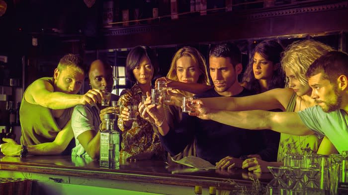 The cast of Sense 8 raising glasses in a toast at a bar.