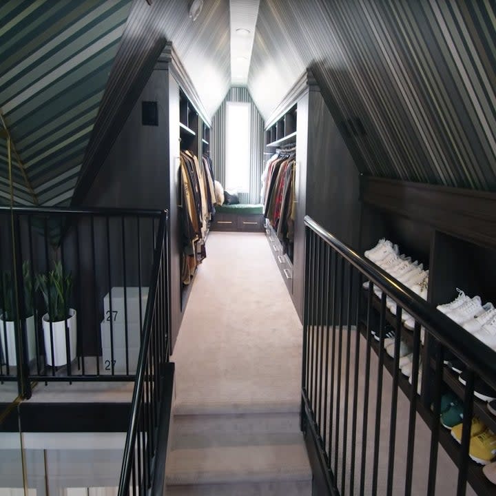 A carpeted staircase leading to a room with slanted ceilings with striped wallpaper