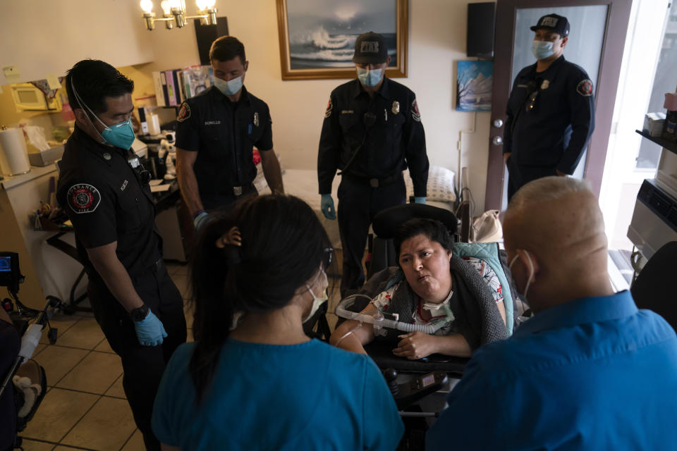 Socorro Franco-Martinez, seated, who has muscular dystrophy, is surrounded by Torrance firefighters as she talks with pharmacist Stella Kim, foreground left, after getting her second dose of the Pfizer COVID-19 vaccine in her apartment, Wednesday, May 12, 2021, in Torrance, Calif. Teamed up with the Torrance Fire Department, Torrance Memorial Medical Center started inoculating people at home in March, identifying people through a city hotline, county health department, senior centers and doctor's offices, said Mei Tsai, the pharmacist who coordinates the program. (AP Photo/Jae C. Hong)