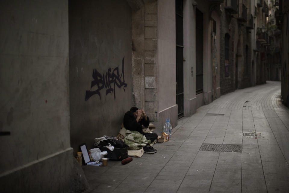 In this Saturday, March 21, 2020 photo, Javier Redondo, 40, covers his head with his hands as he waits for alms on an empty street in Barcelona, Spain. While authorities are telling people to stay at home amid the COVID-19 outbreak, others as Javier are having to stay on the street -- because they have no choice. "I am not afraid of the virus because my physical condition is very good. If I caught the virus, my body would expel it as if it were a gastroenteritis", Javier said. (AP Photo/Emilio Morenatti)