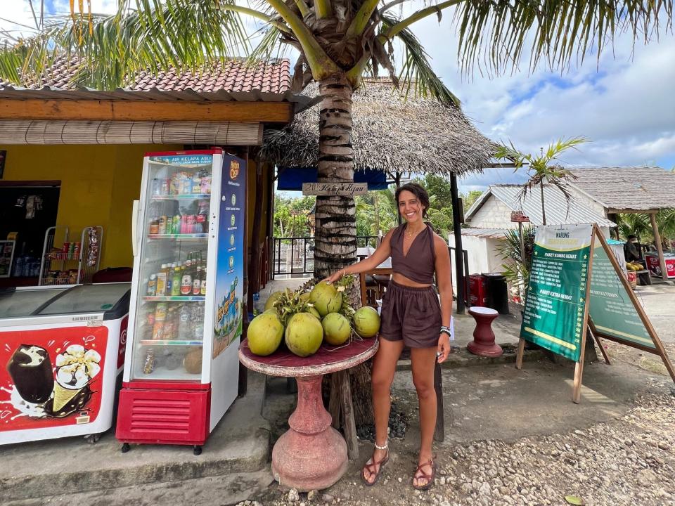 latifah smiling next to a pile of coconuts on a beach