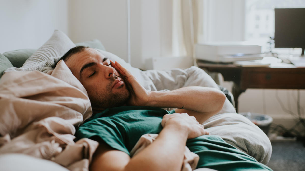  A sleep deprived man in a green shirt falls asleep for a second on his sofa, having what experts refer to as a microsleep because he's sleep deprived. 