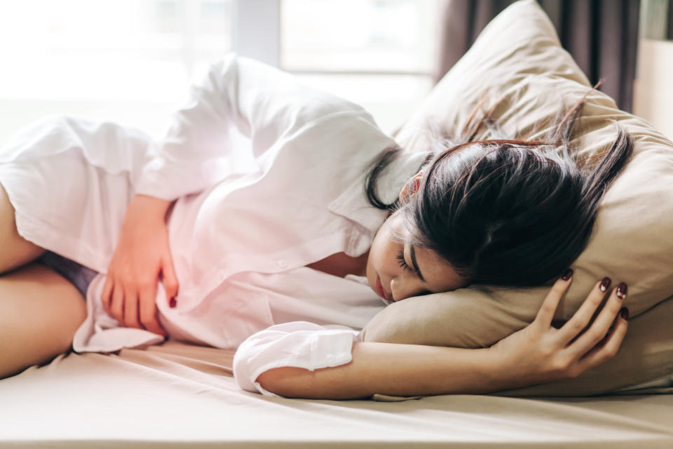 Woman holding onto her stomach in pain in bed (Getty Images)