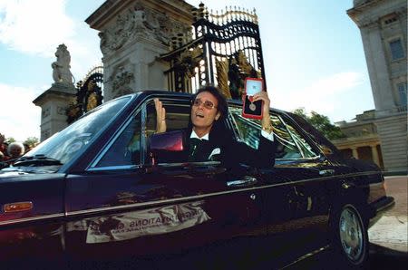 Pop star Cliff Richard shows off his medal as he leaves Buckingham Palace after picking up his knighthood from the Queen, in London, Britain October 25, 1995. REUTERS/Dylan Martinez