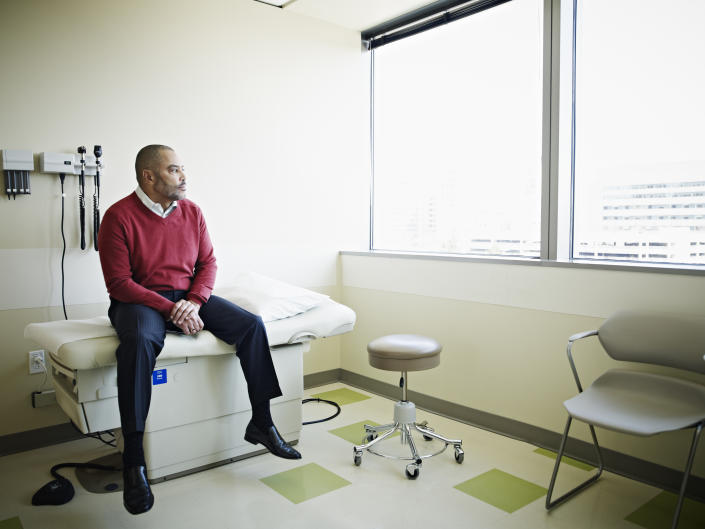 A man sitting on a bed in an exam room looks out the window.