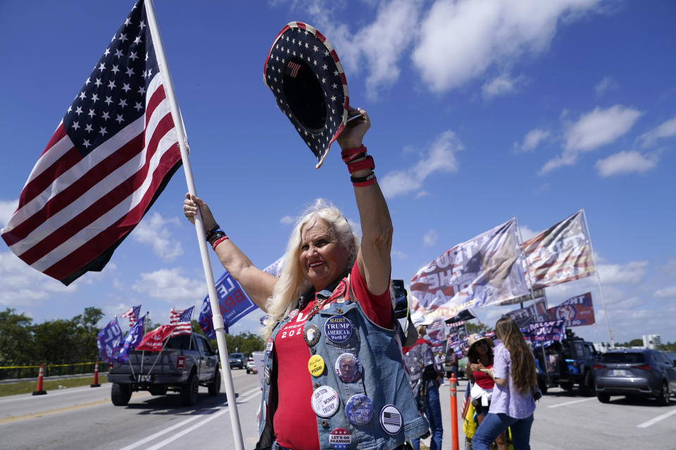 FILE - Kathy Clark, a supporter of former President Donald Trump, waves to passersby outside of Trump's Mar-a-Lago estate, March 21, 2023, in Palm Beach, Fla. The indictment against former President Donald Trump involving a payoff to suppress claims of an extramarital affair is raising concerns that it could undermine public confidence in what many see as far more important investigations into whether he attempted to overturn the results of the 2020 presidential election. (AP Photo/Lynne Sladky, File)