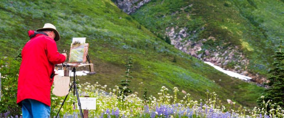 Artist outside in the field painting on his easel a landscape of the wildflowers in the mountains.  Copy space.