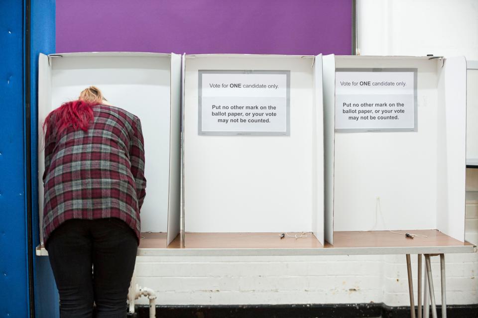 Wirral, UK. 12 December 2019. An early, busy start to the polls as polling stations across the UK open for the General Election, the first to be held in December since 1923. Pictured is a lone voter filling out their ballot paper next to two empty polling booths. Credit: Paul Warburton/Alamy Live News