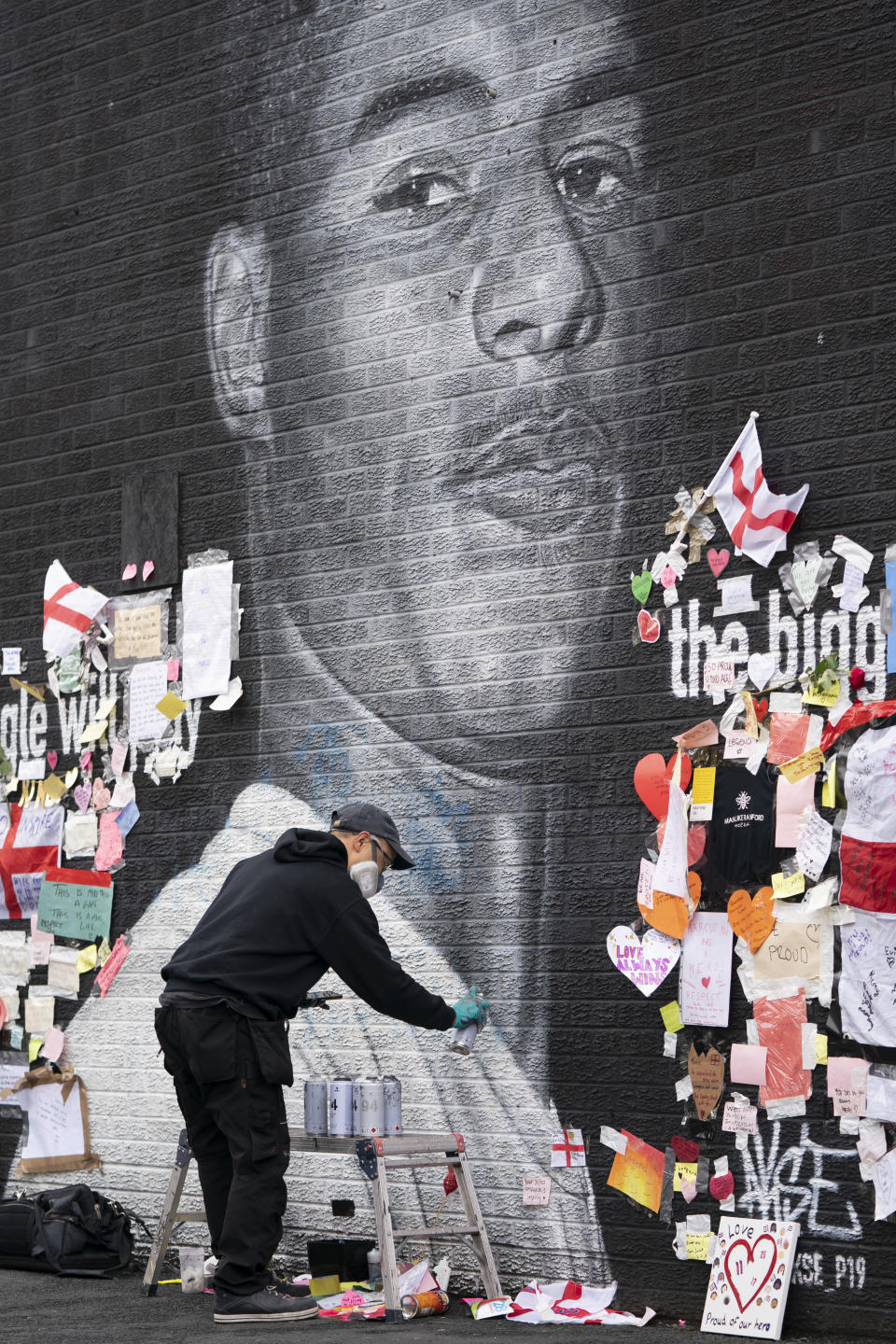 Street artist Akse P19 repairs the mural of Manchester United striker and England player Marcus Rashford on the wall of the Coffee House Cafe on Copson Street, in Withington, Manchester, England, Tuesday July 13, 2021. The mural was defaced with graffiti in the wake of England losing the Euro 2020 soccer championship final match to Italy, but subsequently covered with messages of support by well wishers. (AP Photo/Jon Super)