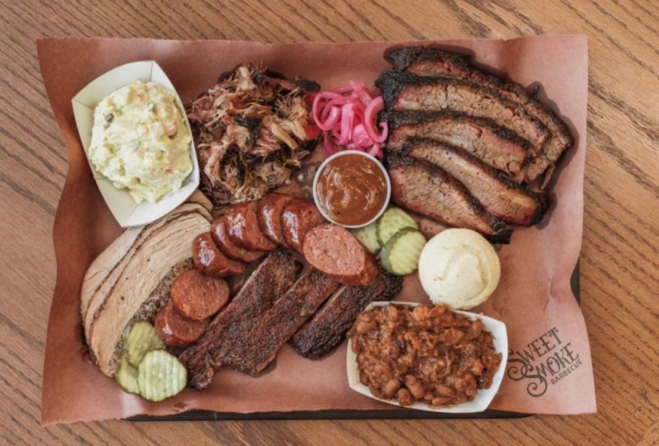 A platter of Sweet Smoke Barbecue's meats and typical sides, served with pickles, pickled onion and barbecue sauce on the side.