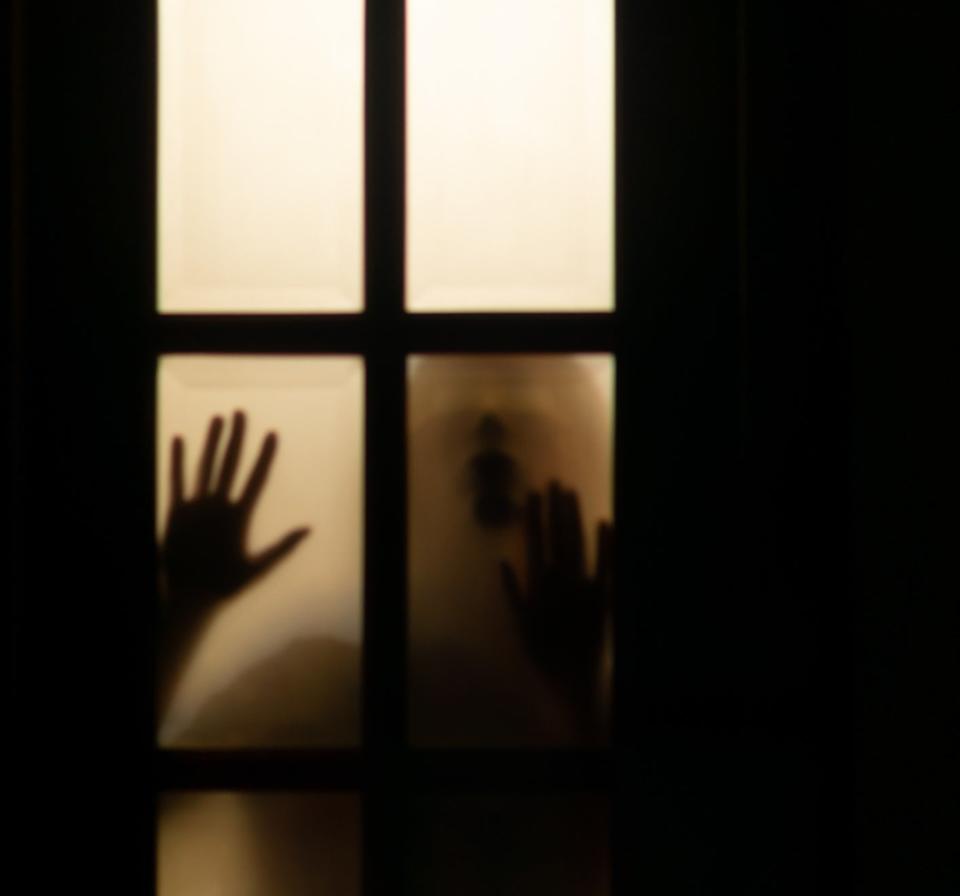 Silhouette of someone with their hands pressed against a window
