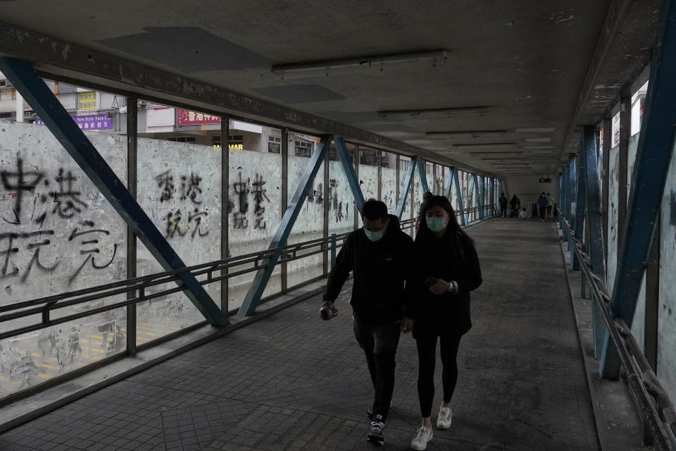 In this Monday, Feb. 10, 2020, photo, a couple wearing protective face masks walks past peeled off posters made by pro-democracy protesters at a footbridge in Hong Kong. The city's often-tumultuous street protests had already slowed in the past two months. Now they have ground to an almost complete halt as attention focuses on how to avoid a recurrence of the SARS pandemic, which killed about 300 people in Hong Kong in 2002-03. (AP Photo/Vincent Yu)