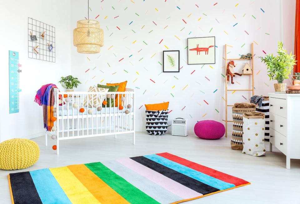 Colorful nursery room with a crib, storage shelves, and a rainbow-striped rug. No persons present