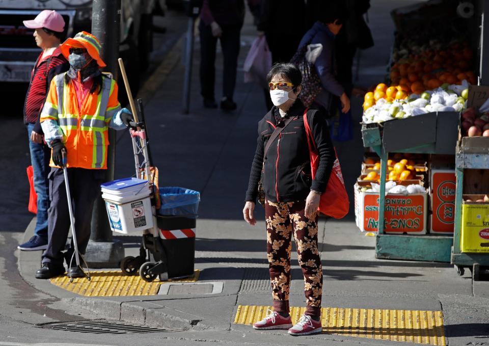 A masked worker and shopper wait for a street signal on Jan. 31, 2020, in the Chinatown district of San Francisco.